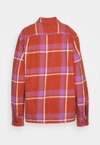 Chemise orange à manches longues avec motif à carreaux violet et blanc, poignets boutonnés et couture de recouvrement au dos, présentée de dos.