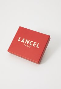Rød rektangulær boks med glatt tekstur, som har "LANCEL" og "PARIS" i gullbokstaver på den øverste overflaten.
