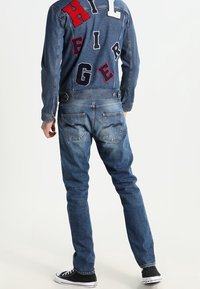 Farkkutakki, jossa on värikkäitä eläimiin viittaavia päällysteitä ja takana teksti "HILFIGER", yhdistettynä sinisiin farkkuihin ja mustiin lenkkareihin. Yksinkertainen rakenne, rento malli.