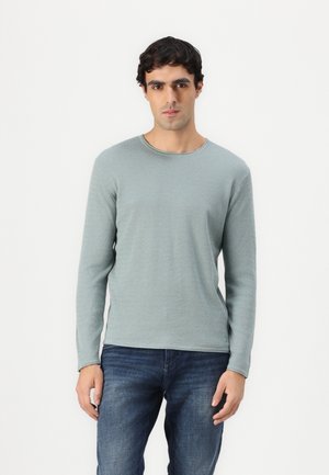 Light teal long-sleeve shirt with a textured fabric and round neckline, paired with dark blue jeans.