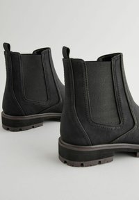Botas negras de tobillo con un exterior suave, paneles laterales elásticos y acentos texturizados. Suelas de goma resistentes con detalle de relieve.
