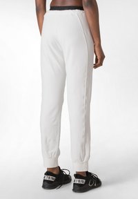 Witte joggers van zachte stof, met een zwarte elastische tailleband en omgezoomde pijpen, gecombineerd met zwarte sportschoenen met logo-accenten.