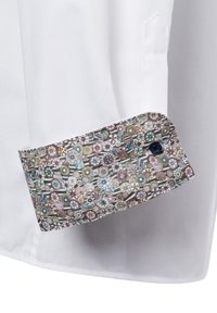 Witte shirt met een gemusterde manchet met cirkelvormige ontwerpen in groene, roze en bruine tinten. De knop op de manchet is marineblauw.