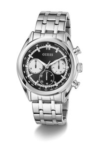 Montre bracelet en métal argenté avec un cadran noir, trois petits cadrans, des marquages de tachymètre et le logo Guess au centre.