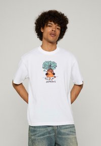 Bílý bavlněný tričko s kresleným motivem postavy pod stromem, se slovem "market" v tmavě hnědé barvě. Krátké rukávy a volný střih.