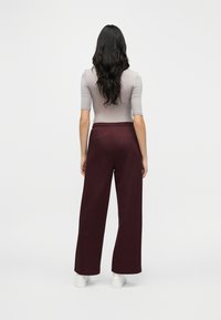 Μπορντό παντελόνι με φαρδιά μπατζάκια και ελαστική μέση, σε συνδυασμό με εφαρμοστό γκρι τοπ. Λεπτή υφή, λιτός σχεδιασμός και μήκος μέχρι τον αστράγαλο.