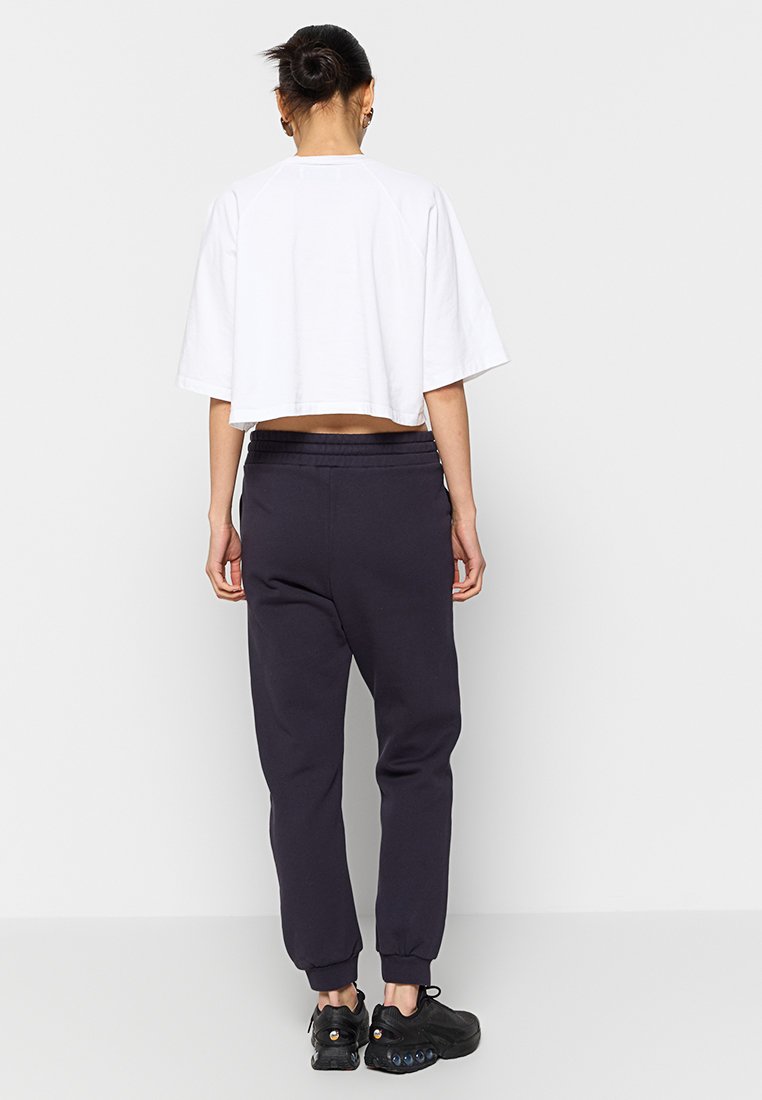 Przycięta biała koszulka z krótkim rękawem, zestawiona z ciemnoszarymi spodniami dresowymi, charakteryzującymi się luźnym krojem i elastycznymi ściągaczami, noszona z czarnymi trampkami.