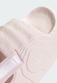 Ružový gumový sklz, hrebienková textura, zaoblené otvorenie a hladký saténový popruh s detailom loga. Dizajn sa zameriava na pohodlie a štýl.