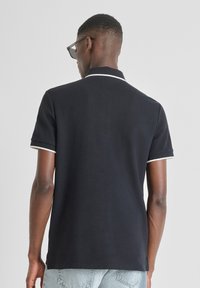 Crna polo majica s jednoličnim dizajnom, kratkim rukavima i bijelim rubovima oko ovratnika i krajeva rukava. Od pamuka, pogodna za svakodnevno nošenje.