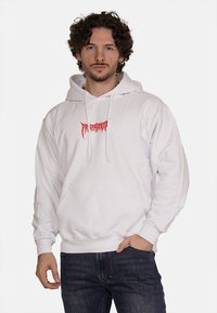 Felpa bianca con grafica rossa sul petto, dotata di tasca a marsupio e coulisse, abbinata a jeans blu scuro.