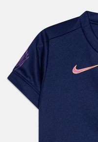 Tumedat sinine sportlik särk lühikeste varrukatega, millel on roosa Nike logo ja ainulaadne roosa disain varrukal. Valmistatud siledast ja hingavast kangast.