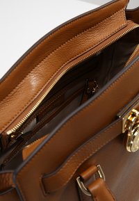 Borsa a tracolla in pelle marrone con cerniera e hardware dorati, che mostra i compartimenti interni e gli slot per carte.