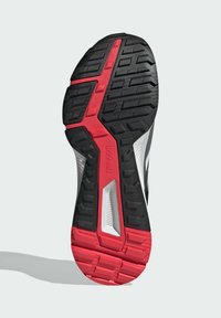 Suela de zapatilla deportiva en negro y rojo con profundos surcos y texto "TRAXION", diseñada para agarre y estabilidad en diversas superficies.