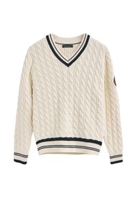 Kremowy sweter z dzianiny w warkocze, z dekoltem w serek oraz granatowymi, prążkowanymi mankietami i brzegiem. Zawiera naszywkę na lewym rękawie.