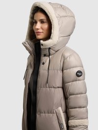 Chaqueta de invierno beige acolchada con capucha forrada de lana, detalles en negro, cierre frontal con cremallera y bolsillos laterales con ribete suave.