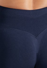Marinblå höga leggings med rippad midja, mjuk textur och sömlös design, med ett chevronmönster nära midjan.