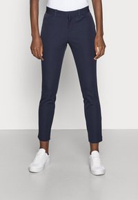 Navy stretch trousers with a tailored fit and tapered legs, featuring side pockets and a smooth waistband, paired with white sneakers.