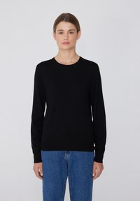 Schwarzer Pullover mit langen Ärmeln und Rundhalsausschnitt, aus glattem Stoff gefertigt. Kombiniert mit blauen Jeans, ergibt einen schlichten, klassischen Look.