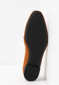 Chaussure à talon en daim marron avec un bout pointu, une semelle en caoutchouc noir lisse et un motif de texture pour une meilleure adhérence.