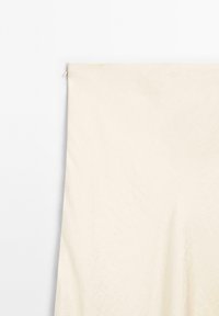 Rideau en tissu couleur crème suspendu contre un fond blanc avec une texture subtile et une apparence légèrement froissée.