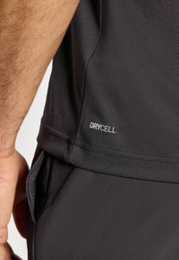 T-shirt de sport noir avec une texture lisse, présentant un petit logo "DRYCELL" sur le côté. Le tissu est léger et évacue l'humidité.