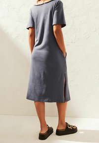 Robe grise à manches courtes avec une coupe décontractée, poches latérales et fentes sur les côtés, faite dans un tissu doux. Associée à des sandales à semelle épaisse et bout ouvert.