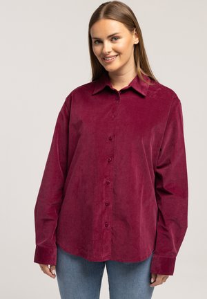 Bordowa koszula z materiału sztruksowego, z kołnierzykiem, długimi rękawami oraz zapięciem na guziki z przodu. Charakteryzuje się gładkim, teksturowanym materiałem i luźnym krojem.