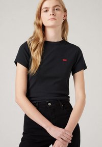 Tricou negru cu dungi, cu mâneci scurte, decolteu rotund și un mic logo Levi's roșu pe partea stângă a pieptului, asortat cu blugi negri cu talie înaltă.