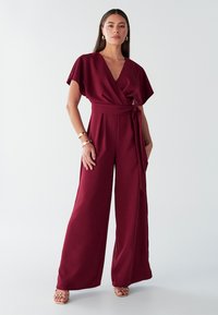 Mono de pierna ancha color granate con diseño cruzado, mangas cortas y cintura anudada. Tela lisa con acabado mate.