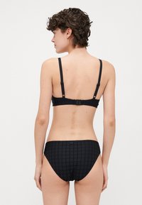 Svart bikini set med en texturerad mönster. Bralette har justerbara axelremmar och en hake-låsning. Bikinibyxorna är låga.