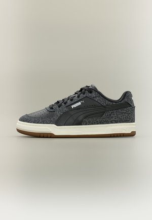 Baskets noires Puma avec un motif léopard foncé, une semelle intermédiaire blanche, une semelle extérieure marron et le logo Puma sur le côté sur un fond uni.