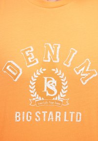 Oranžinė marškinė su baltu spaudu: "DENIM" ir "BIG STAR LTD", su apvaliu lauro vainiku ir retro tekstūra.