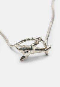 Pendentif en forme de requin en argent sur un collier à chaîne serpent enroulée sur fond blanc.
