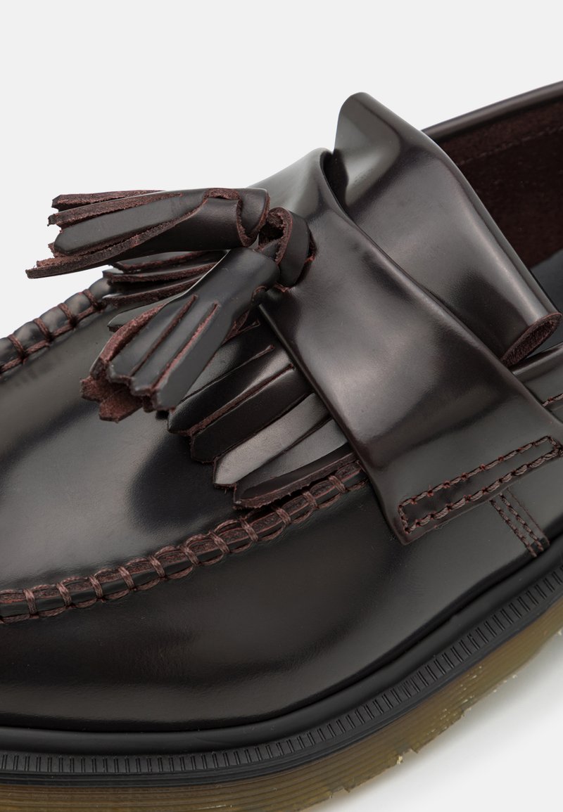 Braune Leder-Mokassin mit runder Spitze, dekorativen Fransenakzenten und genähtem Sohle. Glatte Textur und glänzende Oberfläche.