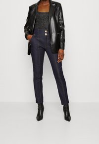 Svart läderblazer över en glittrande svart topp. Mörk denimbyxor med gyllene knappar och synlig sömnad. Svarta ankelboots fulländar looken.