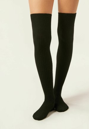 Chaussettes noires côtelées au-dessus du genou avec une texture douce ; conçu ajusté qui s'étend vers le haut, couvrant la partie inférieure de la cuisse et se terminant par des orteils lisses.