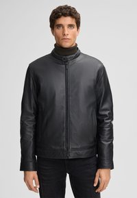 Giacca in pelle nera con colletto rialzato, chiusura frontale con zip e tasche laterali. Presenta una texture liscia e una vestibilità aderente.