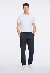 Pantaloni blu navy con una vestibilità rilassata, dotati di cintura con cordino e tasche laterali, abbinati a una maglietta bianca semplice e sneakers bianche.
