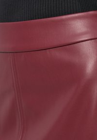 Gonna in pelle bordeaux caratterizzata da una texture liscia, una vita piatta e dettagli di cucitura delicati, che mette in mostra un design sartoriale.