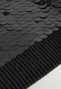 Black rug featuring a textured striped pattern at the base and a layered design of circular scales on top, all in black.