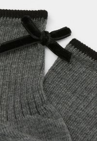 Graue Stricksocken mit gerippter Textur, die an der Oberseite eine schwarze Samtschleife und einen kontrastierenden schwarzen Bund haben.