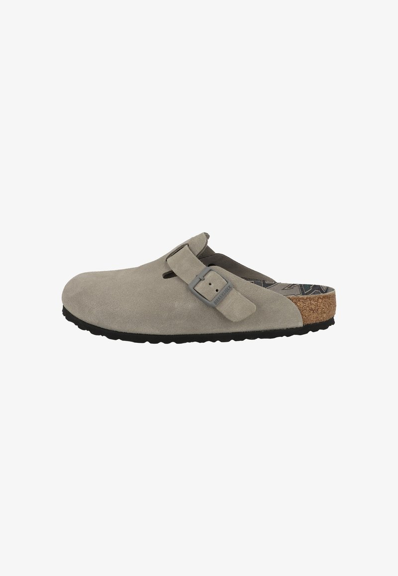 Zoccolo in suede grigio con una fascia laterale e una fibbia. Fodera in sughero e suola in gomma nera, dotato di fori per la ventilazione.