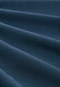 Nahaufnahme eines gefalteten dunkelblauen Stoffs mit einer feinen Fischgrät-Webstruktur, die sanfte diagonale Rillen schafft.