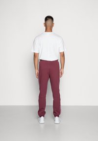 Vinröda sweatpants med vita sidostripes, elastisk midja och avsmalnande ben; bärs med en enkel vit t-shirt. Enkel, avslappnad design.