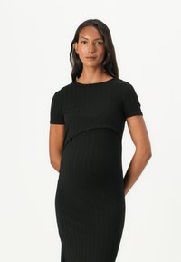 Μαύρο ριμπ φόρεμα εγκυμοσύνης με κοντά μανίκια, εφαρμοστή σιλουέτα και επικαλυπτόμενο σχέδιο στο στήθος για άνεση και στυλ.