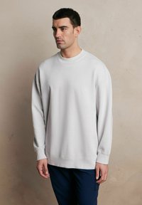 Jasnoszara bluza z okrągłym dekoltem, długimi rękawami i ściągaczami. Miękka tekstura i luźny krój, połączona z granatowymi spodniami.