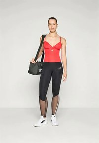 Red athletic tank top with thin straps, black leggings featuring mesh accents and white stripe details, paired with white sneakers and a black bag.