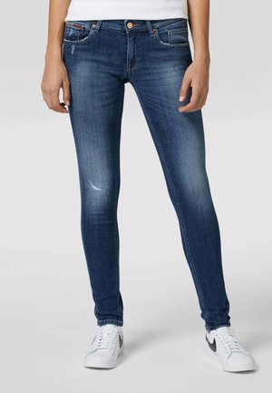 Slim fit modré džíny s lehkým opotřebením na levém stehně, doplněné bílými teniskami s černými logy Swoosh.