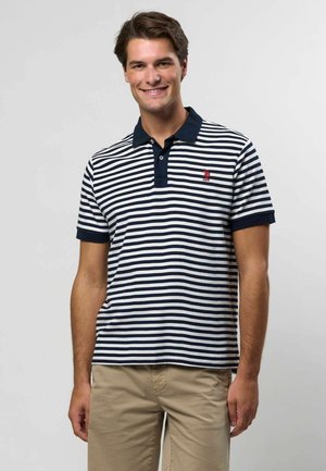 Jūroje ir baltame dryžuotas polo marškinėliai su tvirtu jūrinės spalvos apykakle ir rankogaliais, kairėje krūtinėje esantis mažas raudonas logotipas. Kasdienis pasiūlymas.