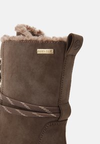 Botte d'hiver en daim marron avec doublure en fourrure moelleuse, lacets rayés et étiquette métallique "DUO-TEX" sur le côté.